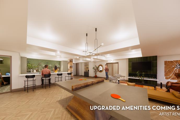 Open-concept apartment community clubhouse with a seating area in the foreground, pool table, and tv area in the rear by a kitchenette